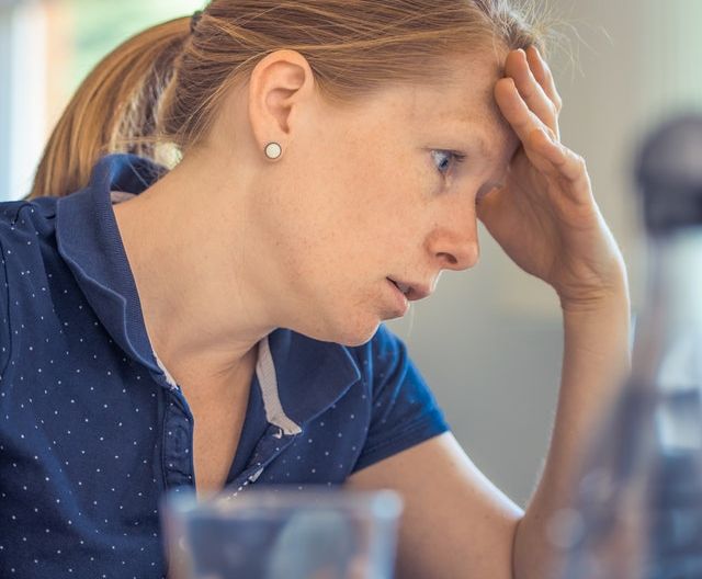 Stressed woman in polka dotted blue shirt with hand over face